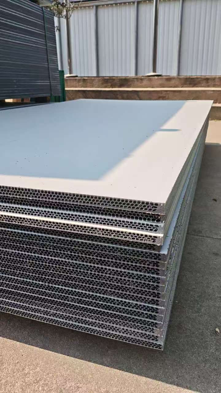 PP hollow plastic formwork panels stacked outdoors revealing honeycomb hollow core structure, metal fence and factory buildings in background