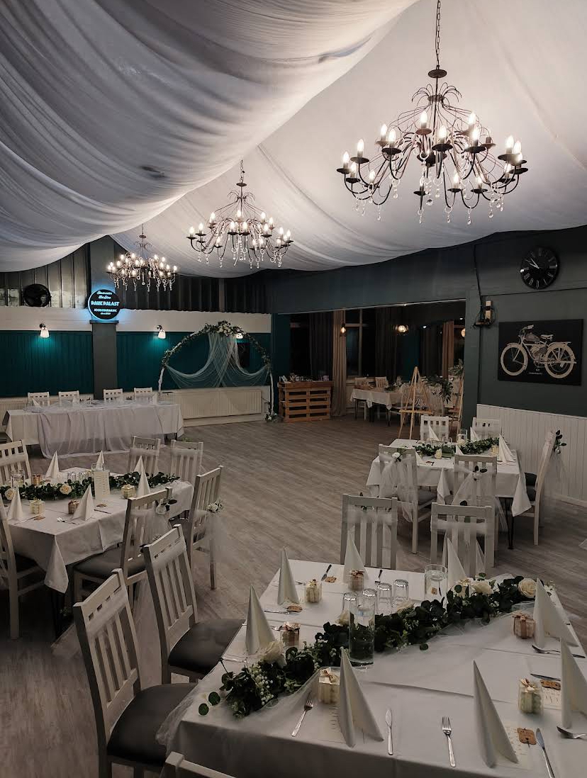 Hochzeitssaal mit weißen Tischen und Kristalllüstern