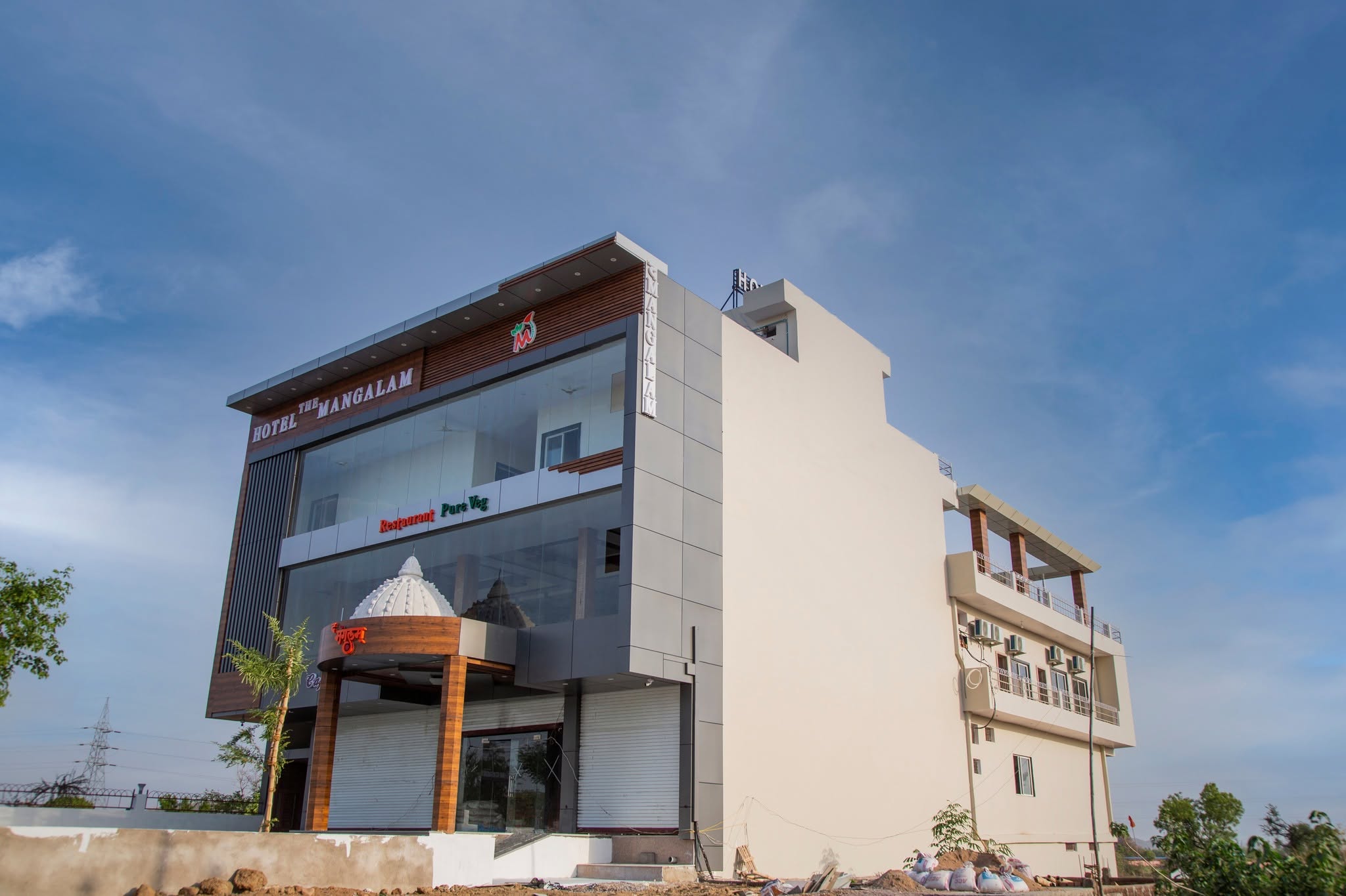 The Mangalam Hotel modern building in daylight showing the fine dining restaurant entrance with Restaurant Pure Veg signage glass facade and decorative dome structure in Nowgong Chhatarpur Madhya Pradesh