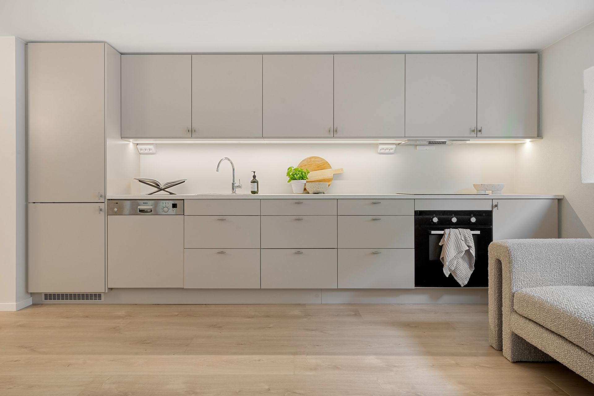 Fertiggestellte moderne Küche mit hellgrauen Fronten, Holzboden und offenem Wohnbereich
