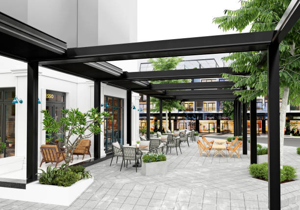 Modern louvered roof pergola system with black adjustable canopy over stone patio with dining furniture and greenery in a commercial setting