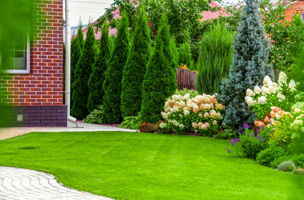 Beautifully designed landscape with red brick building, mature evergreen trees, colorful flower beds, and neatly manicured lawn