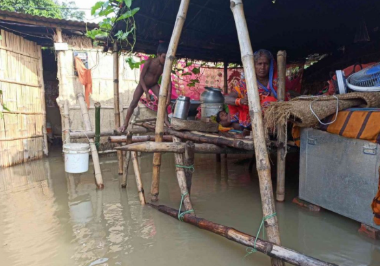 Makeshift bamboo shelter in flooded area with kitchen items and a fan
