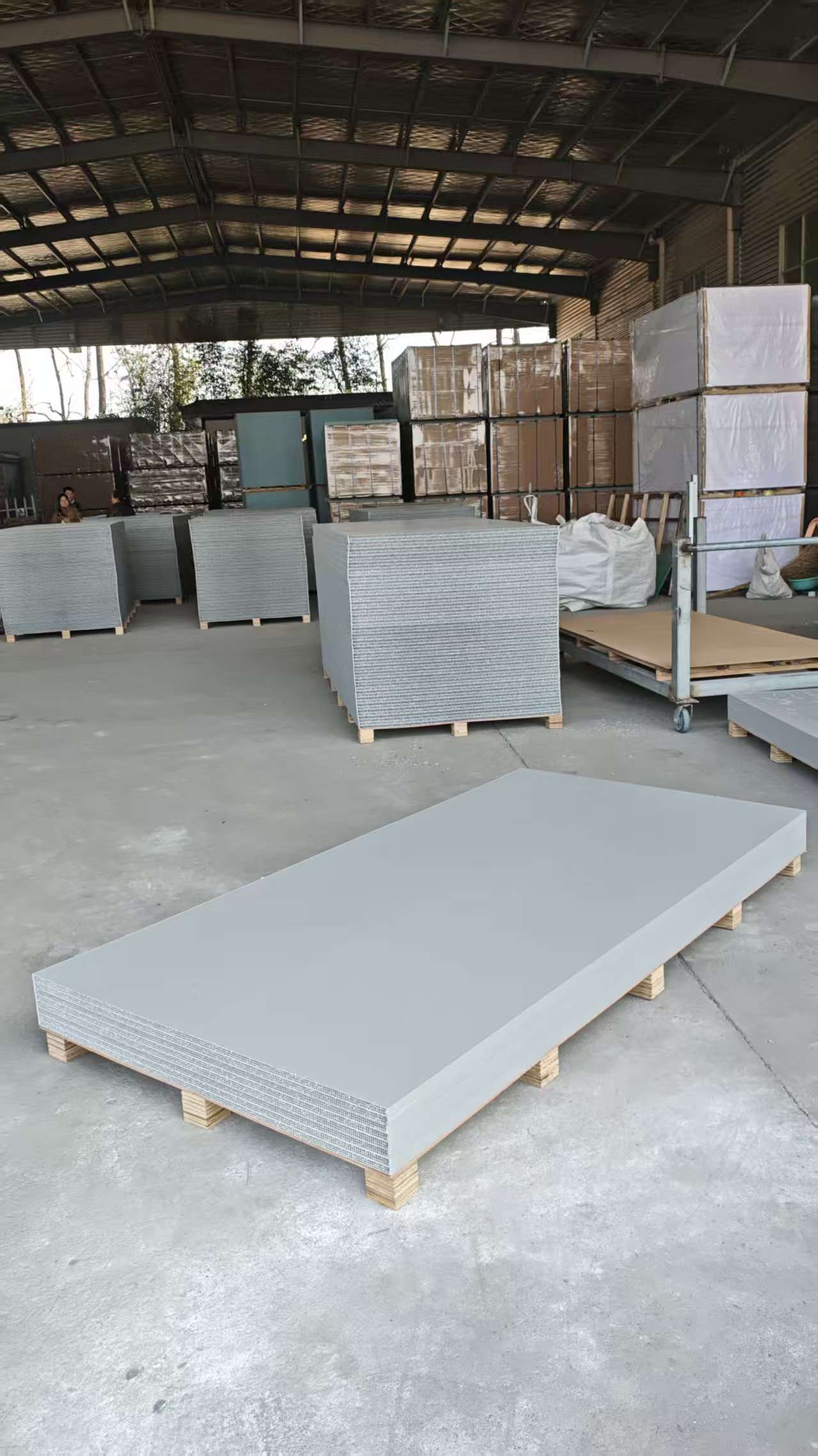 Large factory storage area with stacked grey hollow plastic formwork panels under metal roof