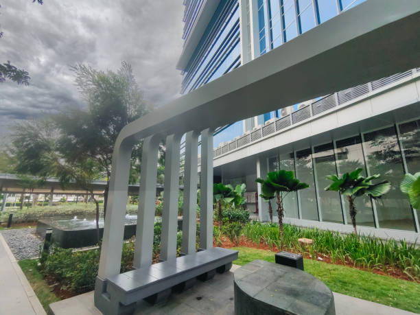 Modern glass curtain wall office building with professionally irrigated outdoor courtyard featuring white metal seating structures, palm trees, manicured shrubs and lawn, small water feature, and lush green landscape maintained by commercial sprinkler system