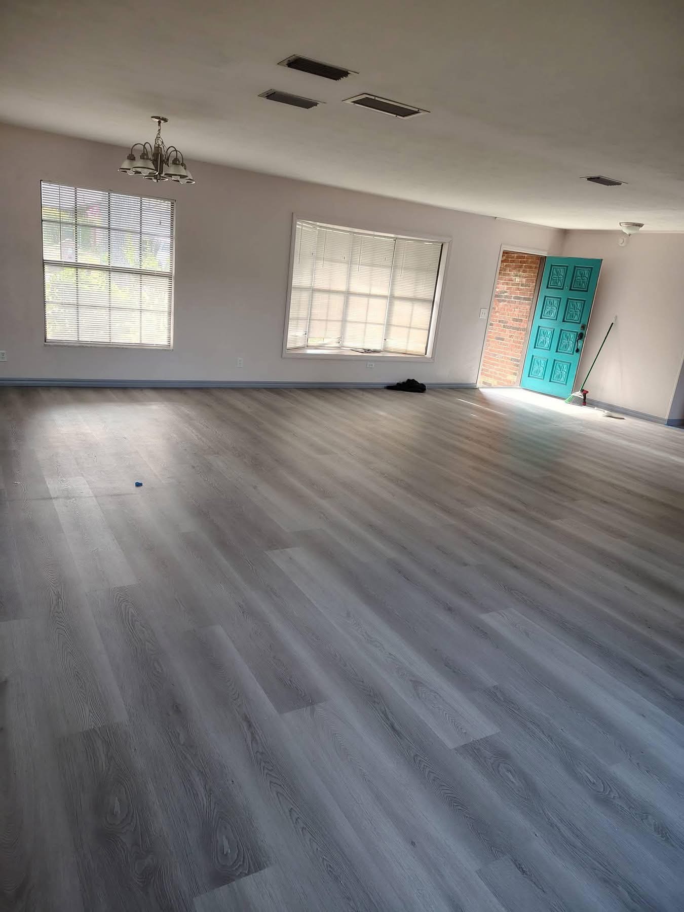 Empty room with light gray wood-look flooring and windows with blinds — seamless plank installation by E P Herrera Construccion