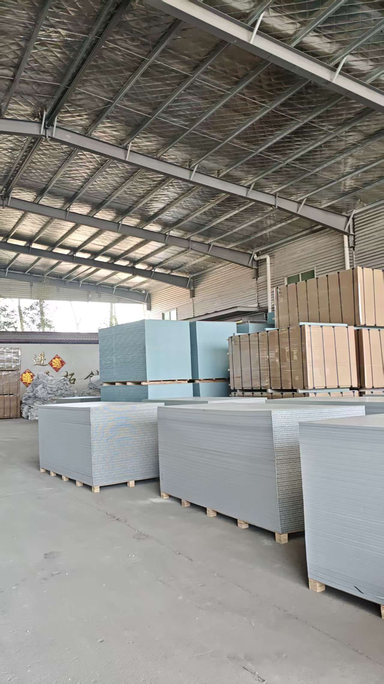 PP hollow plastic formwork warehouse interior with multiple panel colors including light blue, brown and gray neatly stacked on wooden pallets under insulated metal roof