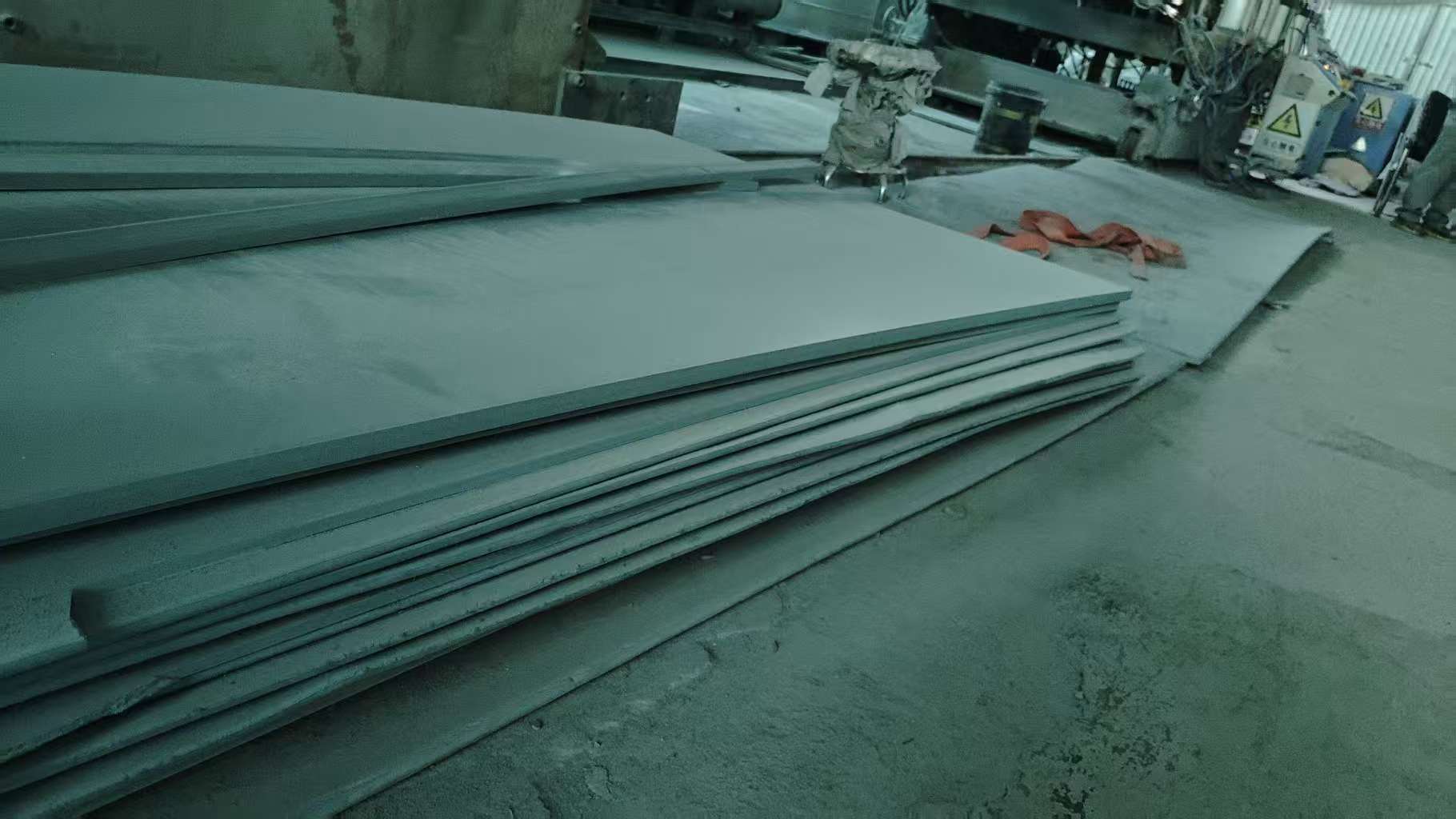 Raw steel plate materials stored in factory production area alongside processing equipment
