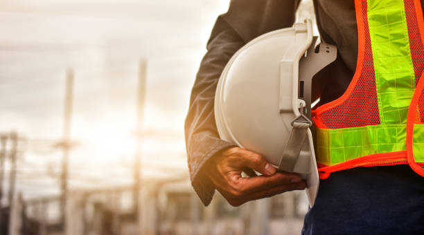 Commercial landscaping professional in orange safety vest and hard hat on site at a business property with buildings in the background