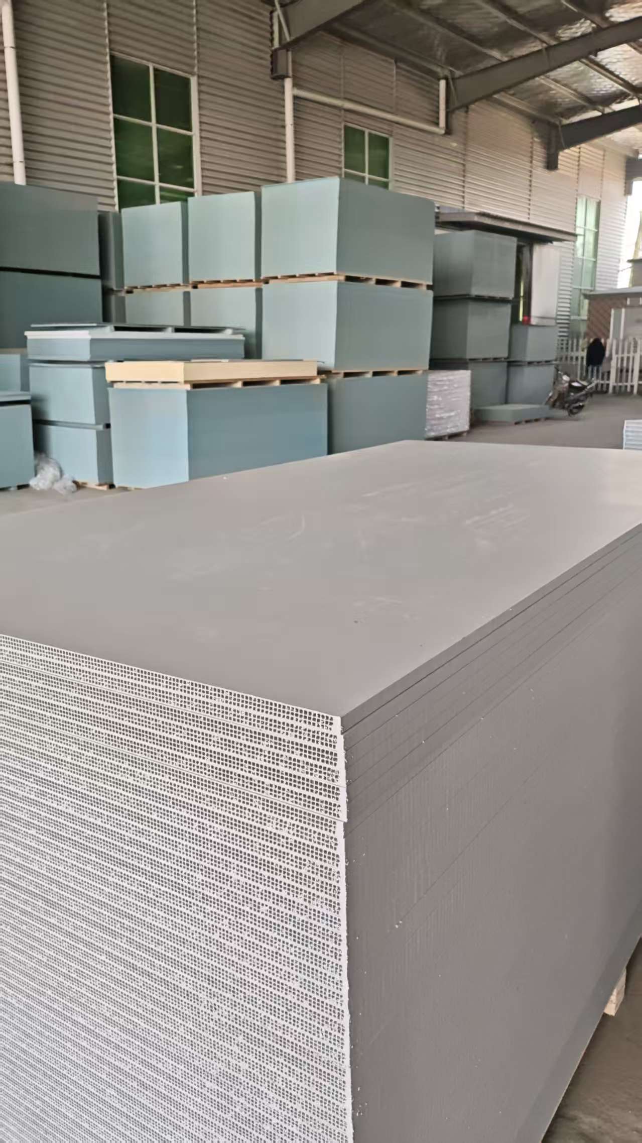PP hollow plastic formwork warehouse storage facility with large stock of gray honeycomb panels in foreground and blue packaging boxes in background, corrugated metal factory walls