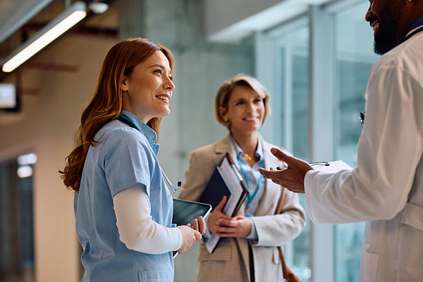 Healthcare medical facility corridor with medical professionals in scrubs and lab coats collaborating, glass partitions and modern lighting in a hospital setting
