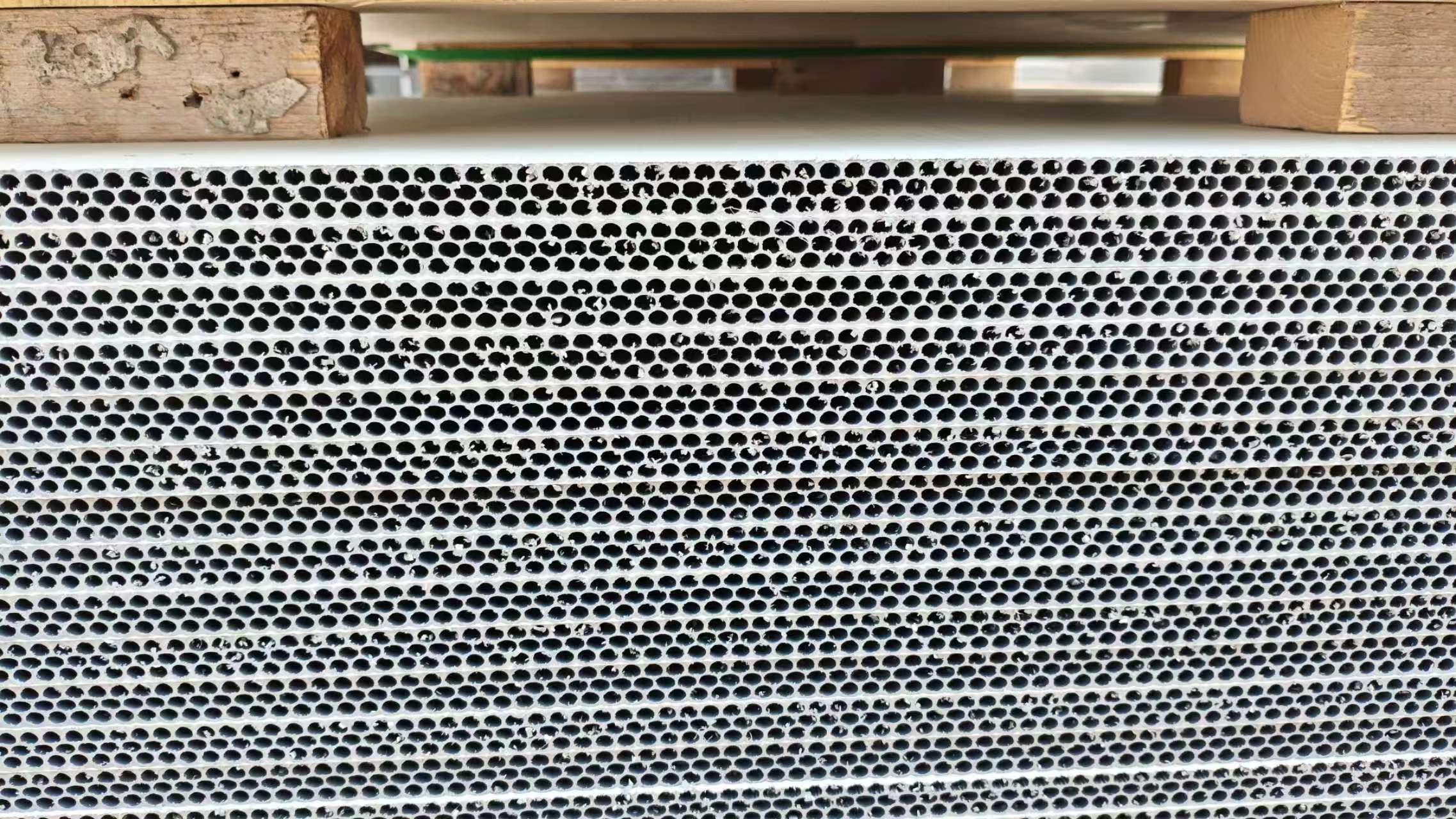 Single PP hollow plastic formwork panel showing dense circular hollow core holes resting on wooden support brackets and pallet in storage area
