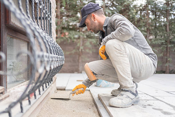 Professional contractor installing commercial pavers near building with fence and landscaping