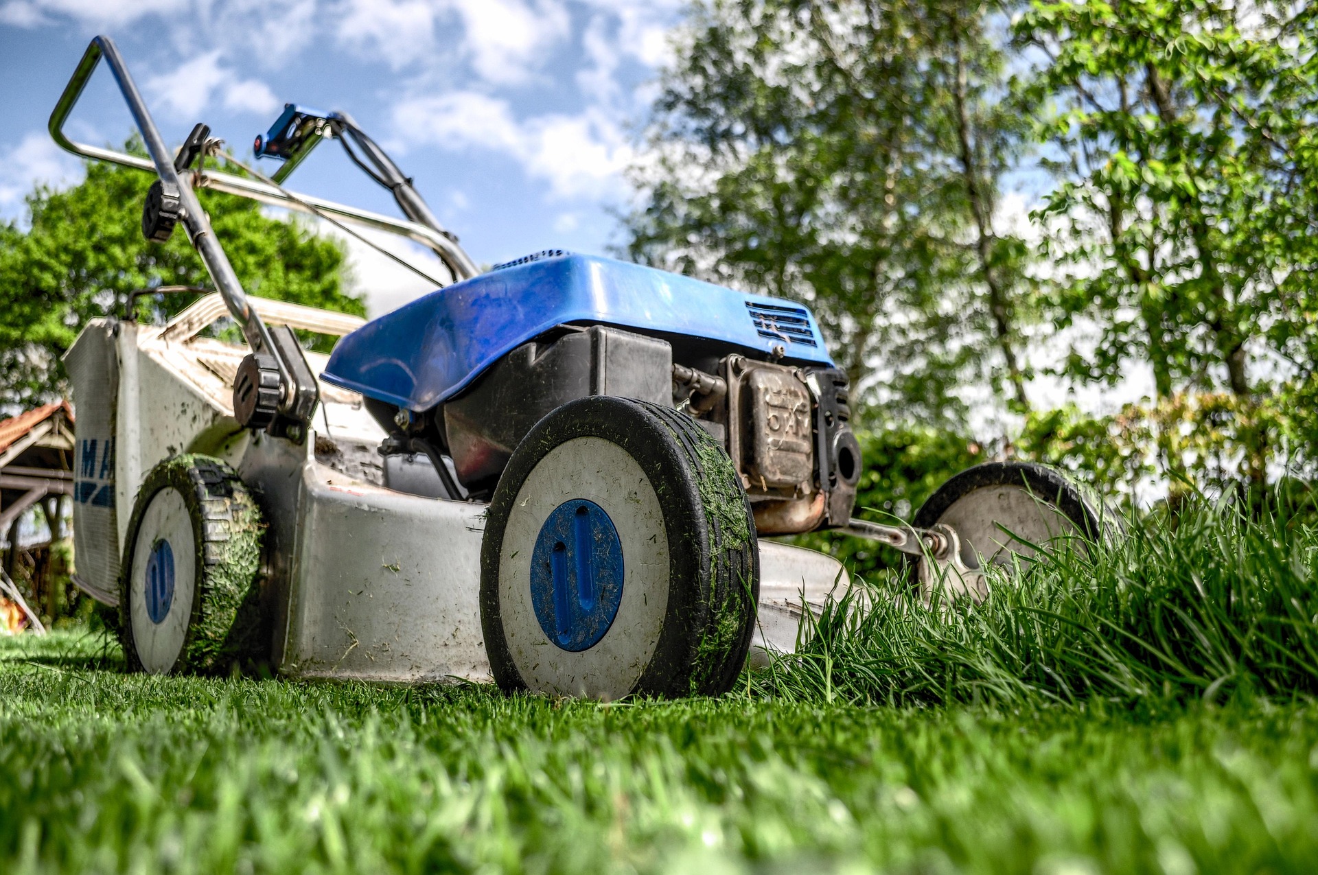 Professional commercial mower on freshly cut green lawn with trees and blue sky in background