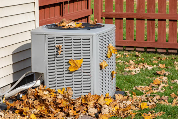 Seasonal yard cleanup showing AC unit surrounded by fallen yellow autumn leaves with red fence and white house exterior during fall