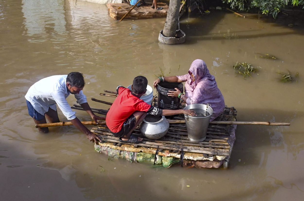 Family on a makeshift bamboo raft carrying metal containers through flood water