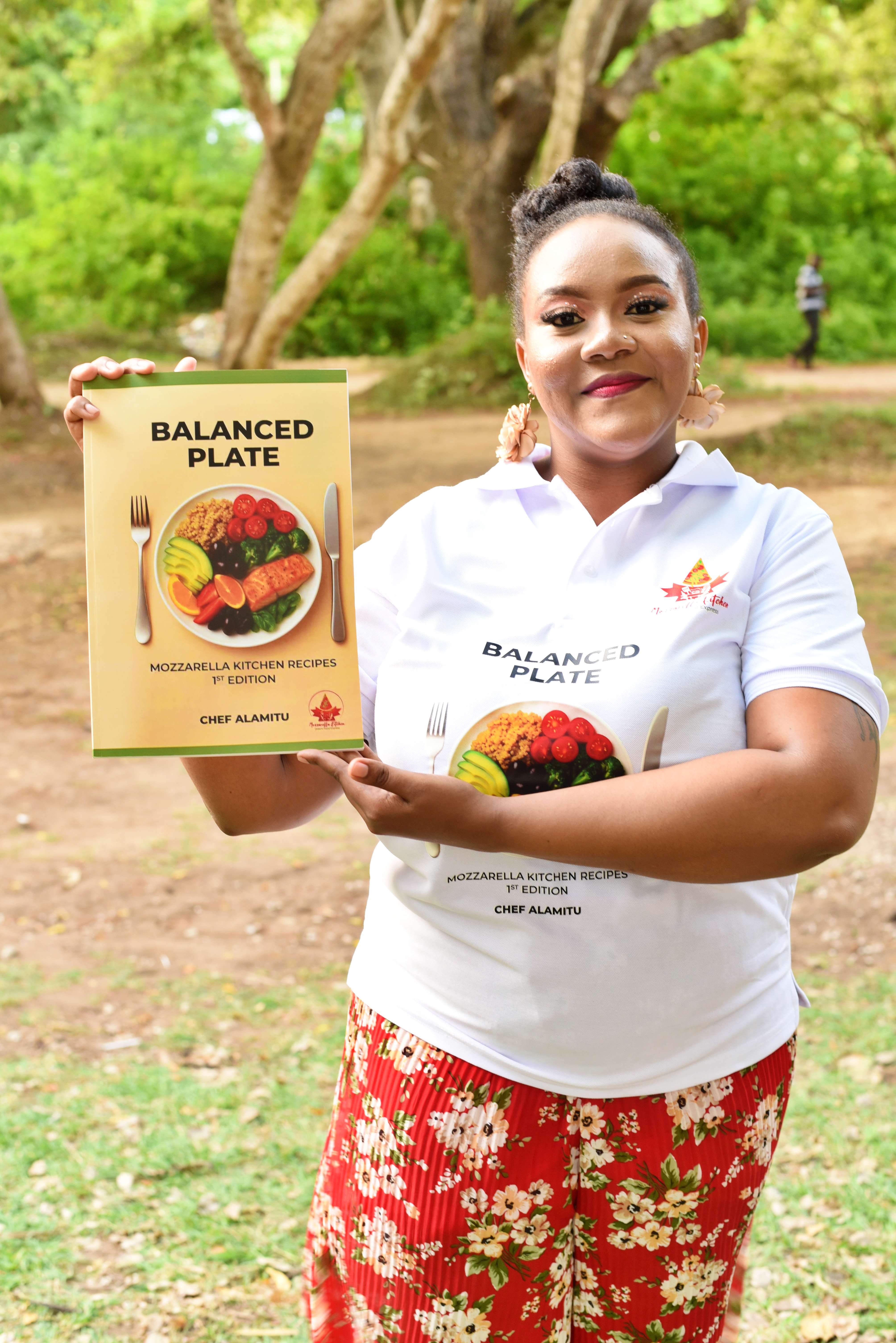 Chef Alamitu holding The Balanced Plate Cookbook