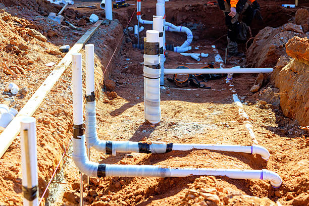Commercial drainage pipe installation in excavated trench with branching white PVC pipes on graded site