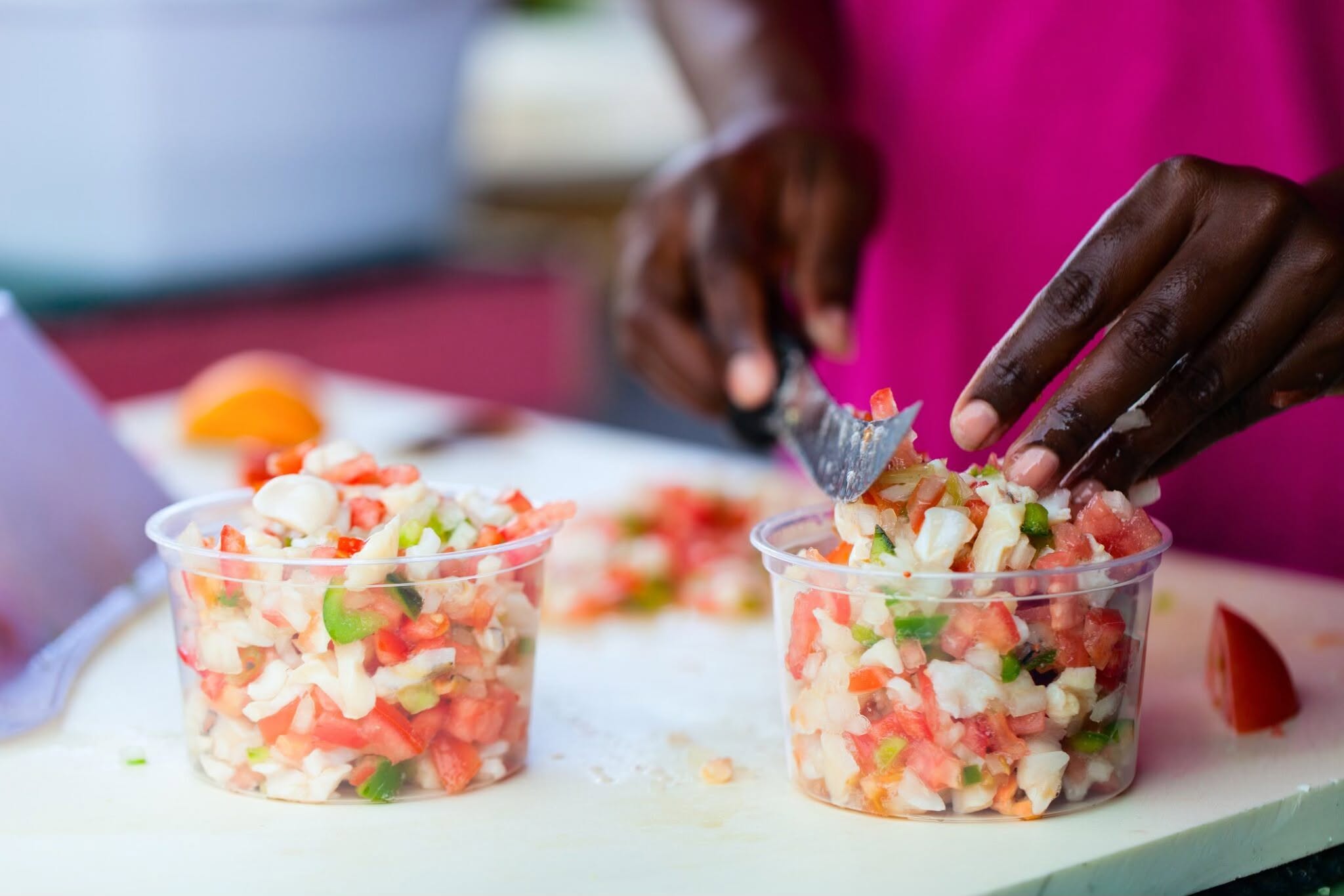 Hands carefully chopping fresh conch, tomatoes, and peppers for a Bahamian salad.