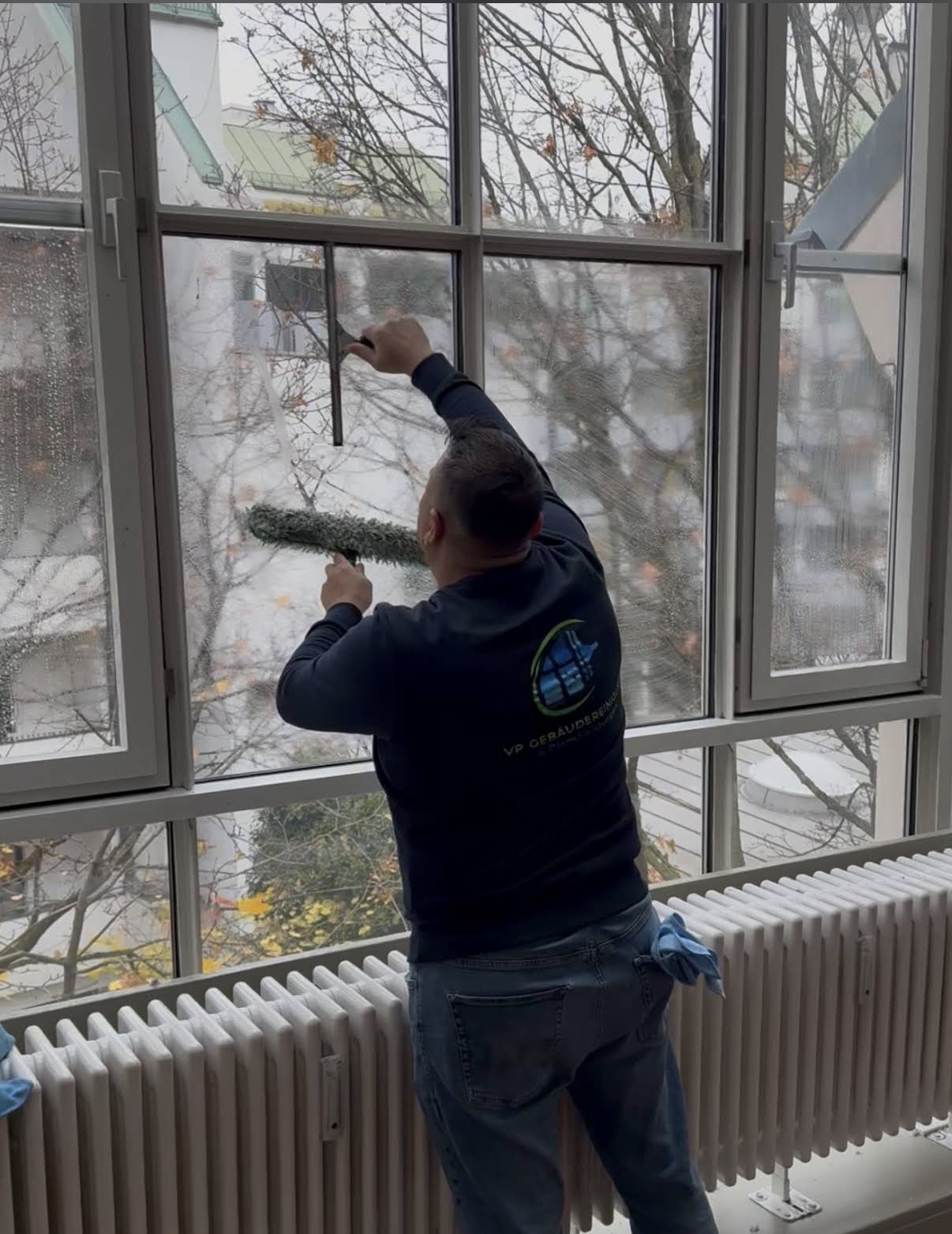 Mitarbeiter von VP Gebäudereinigung reinigt mit Abzieher ein großflächiges Fenster