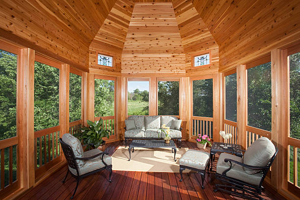 Custom screened gazebo with glass windows, furnished with sofa and armchairs on dark wood floor overlooking wooded garden
