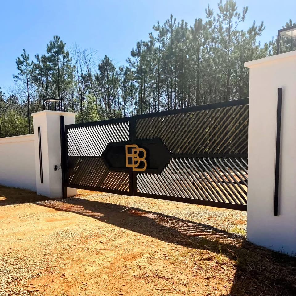 Black openwork gate with gold BB monogram detail set between white pillars under a clear sky