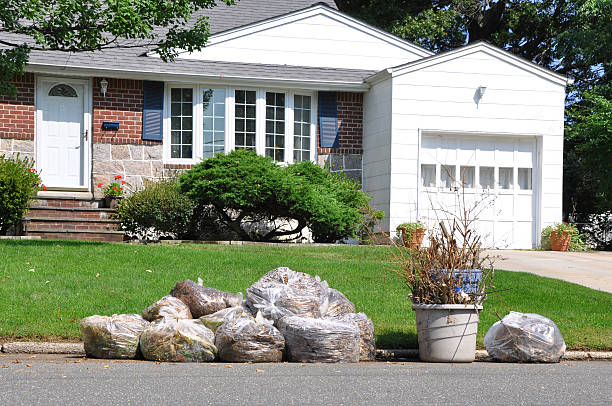 Red and white suburban home with green lawn after professional spring yard clean up, bags of collected yard debris stacked at lawn edge, large planter with healthy plant, mature trees surrounding property on clear sunny day