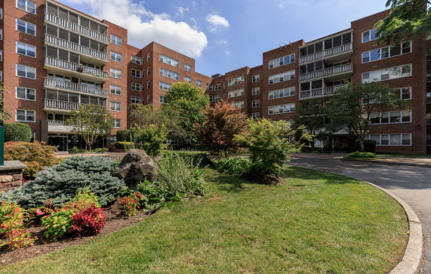 Well-landscaped apartment complex with maintained green spaces, shrubs, trees, and decorative rock features in front of red brick residential buildings