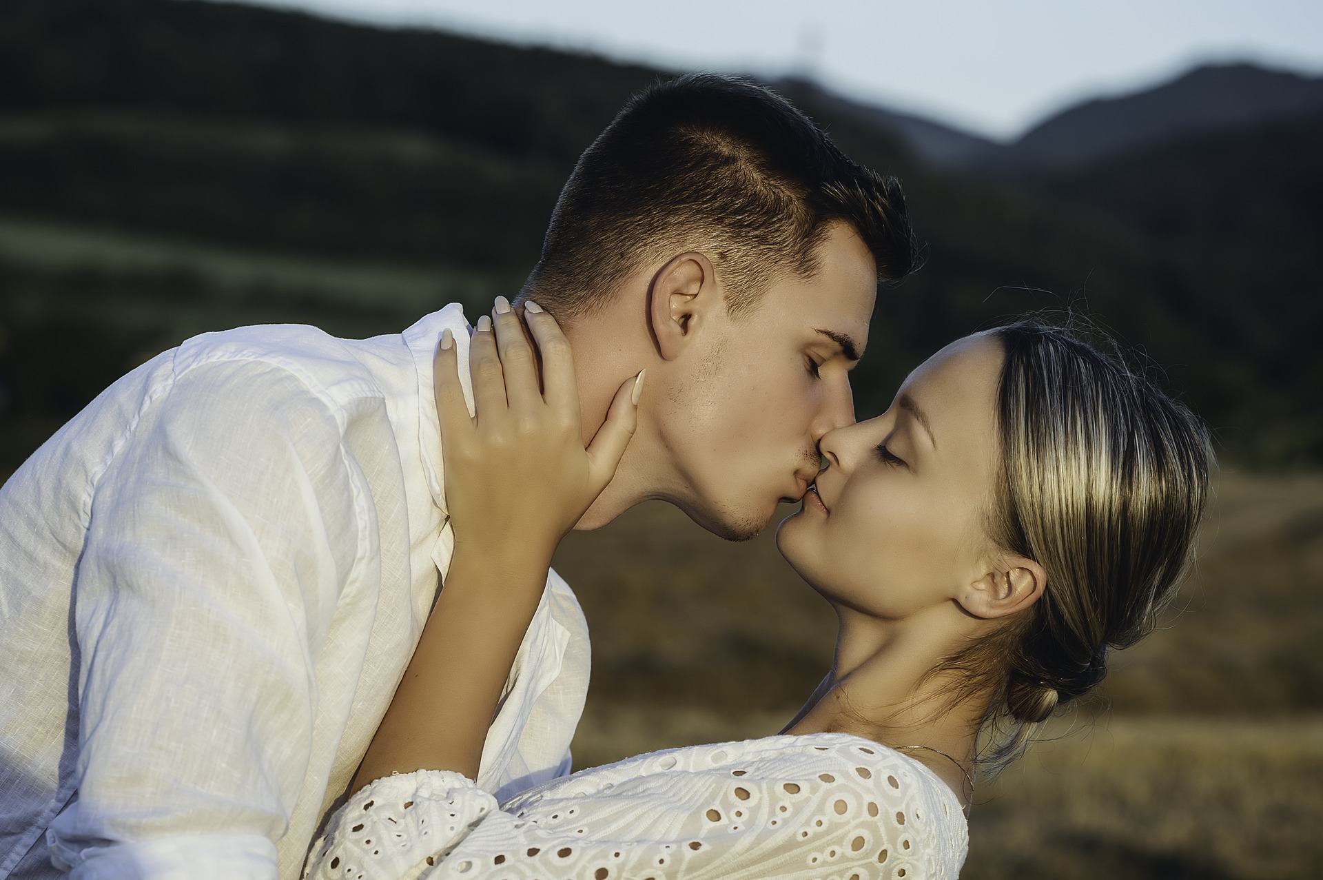 Pár sa bozkáva v prírode — romantická atmosféra, hory a lúka v pozadí