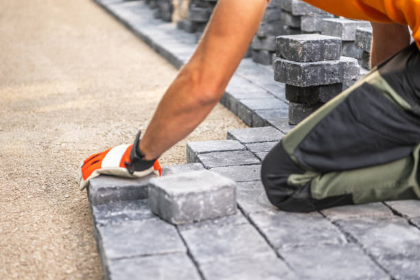 Commercial landscaping worker installing gray paver stones on a prepared sand base for a hardscape walkway or patio at a business property