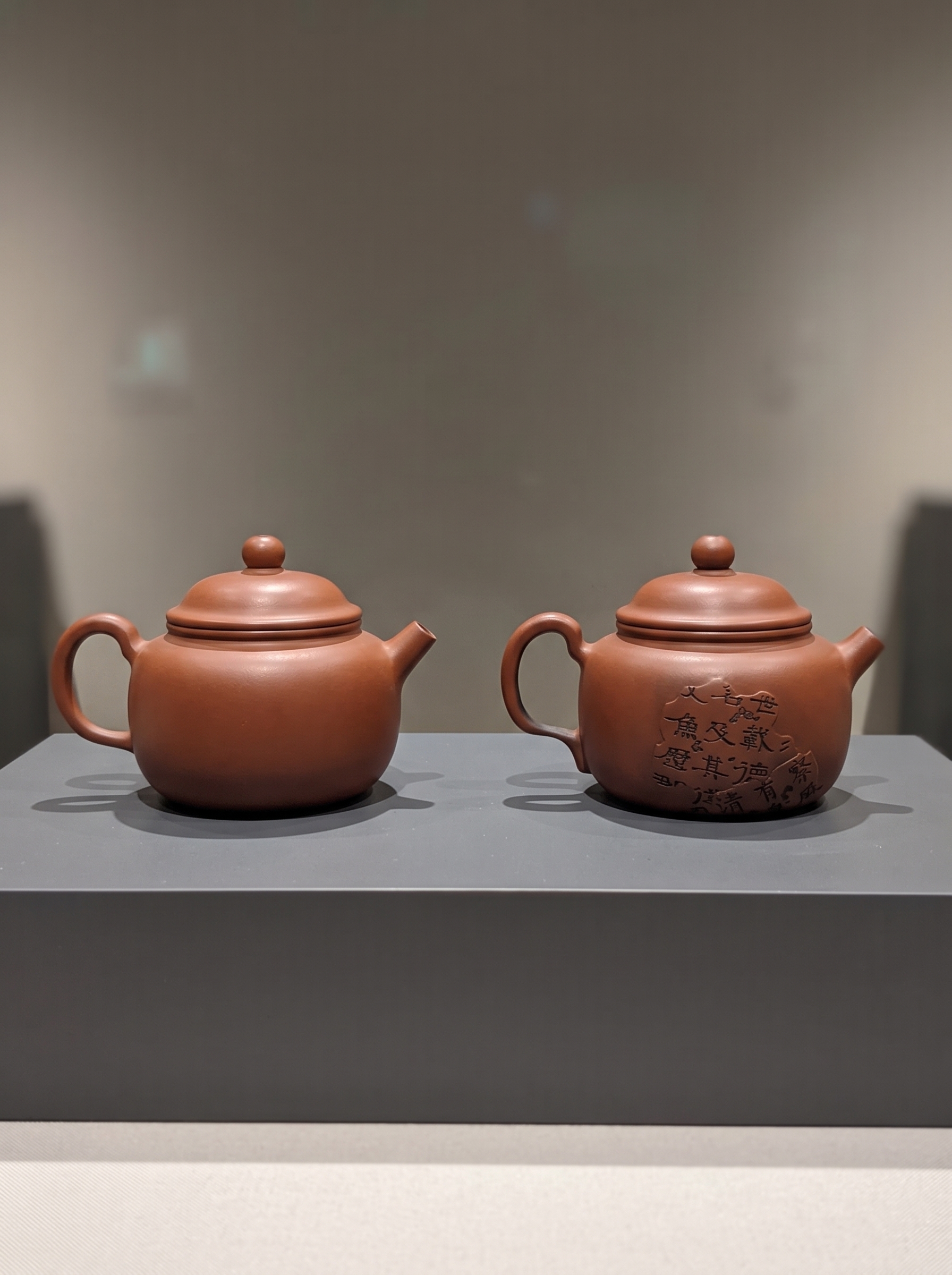 Jianshui Zitao teapots on display — one plain, one carved with calligraphy