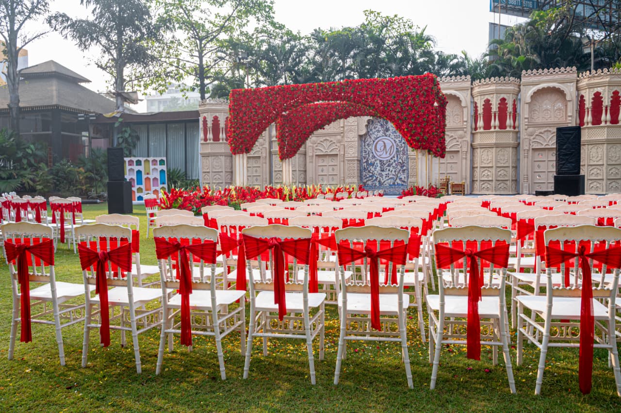 Wedding Lawn in Nashik – White chairs with red ribbons and floral arch at Vrindavan Greens
